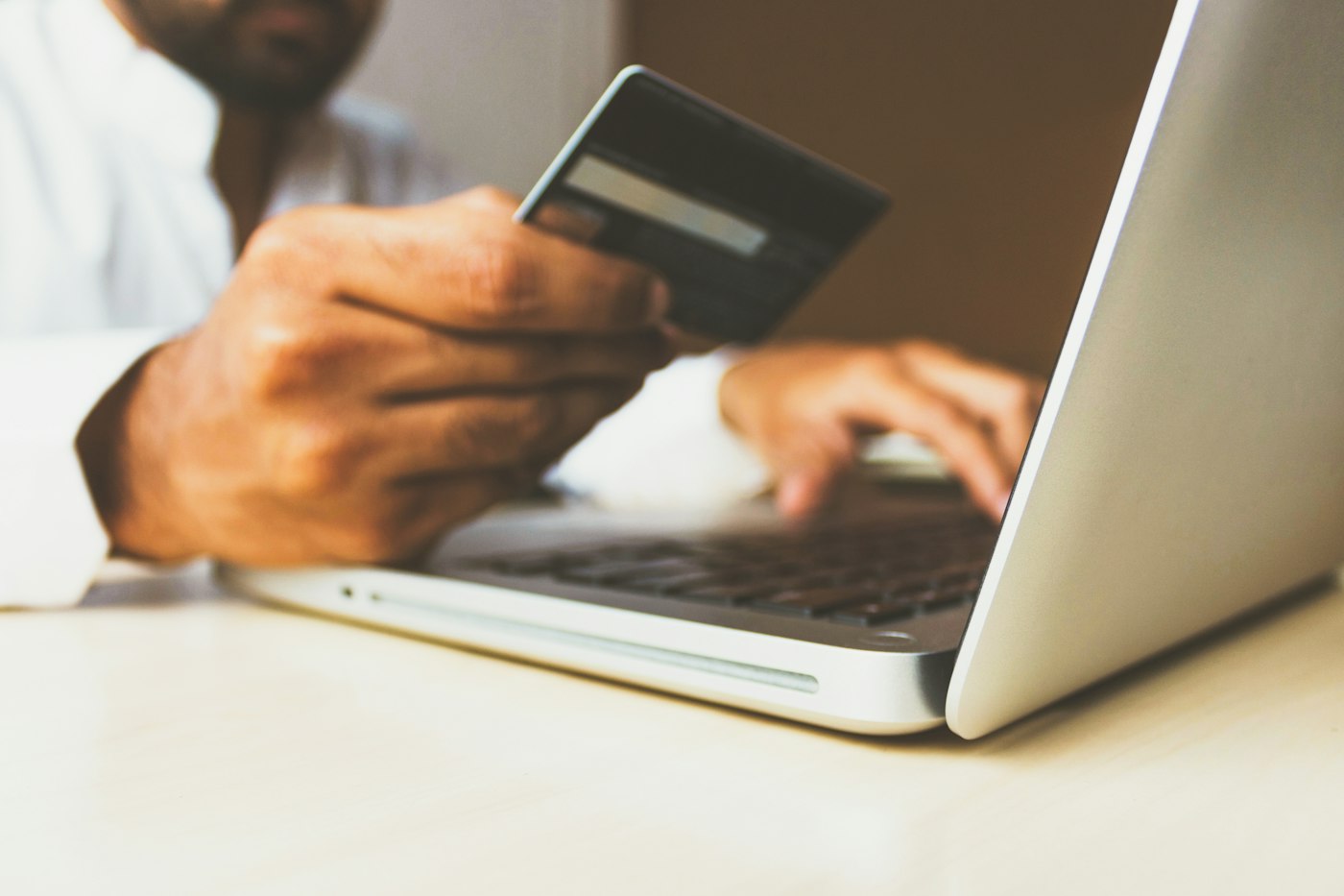 A person shopping online on a laptop with a bank card in hand